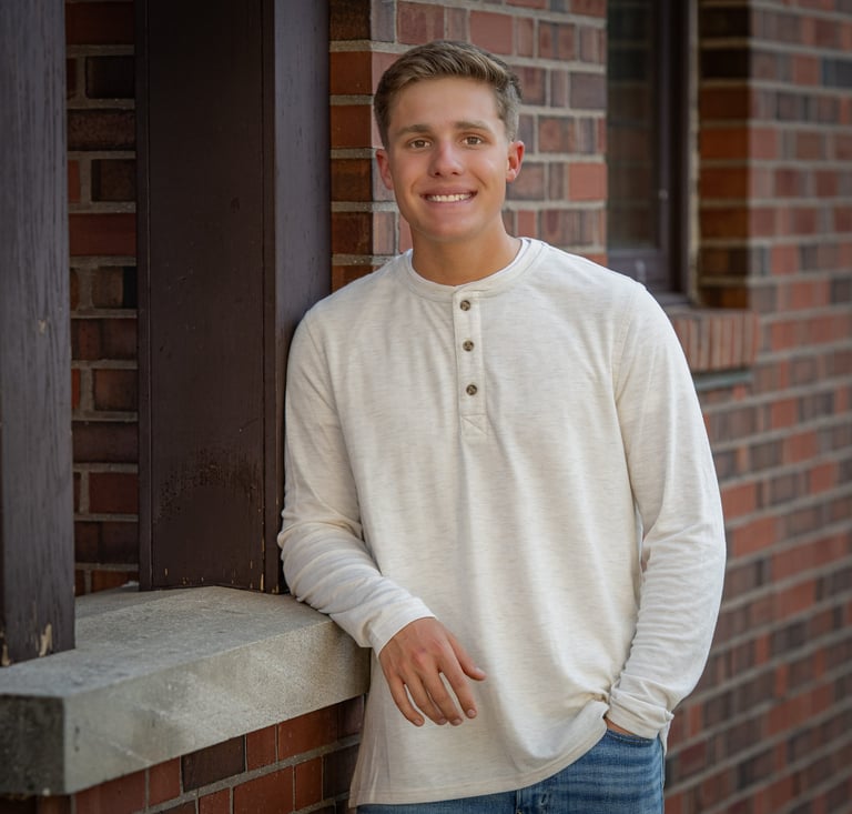 Smiling man in cream henley shirt and jeans leaning against brick wall